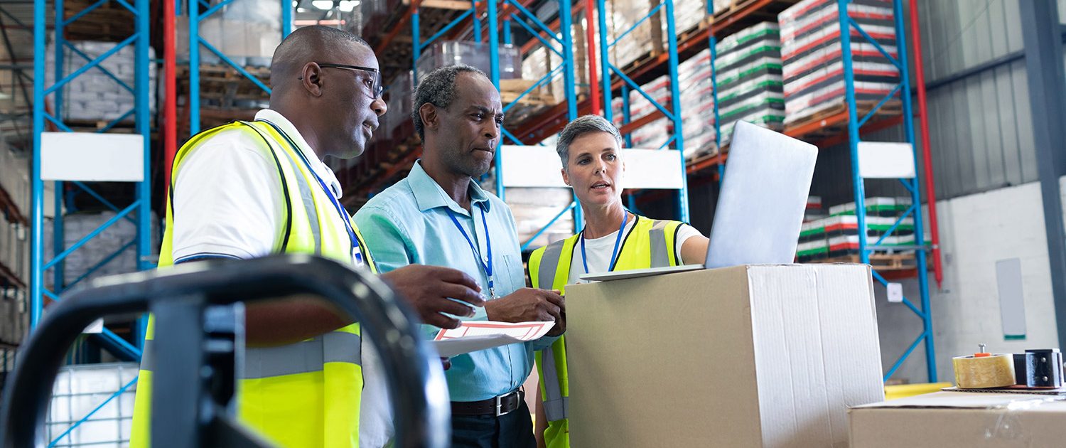 Side view of mature diverse warehouse staffs discussing over laptop in warehouse