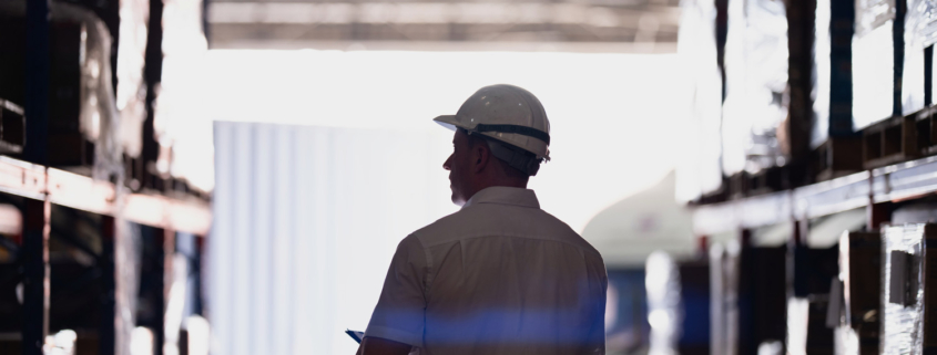 silhouette of a logistics worker with a hardhat walking through a warehouse
